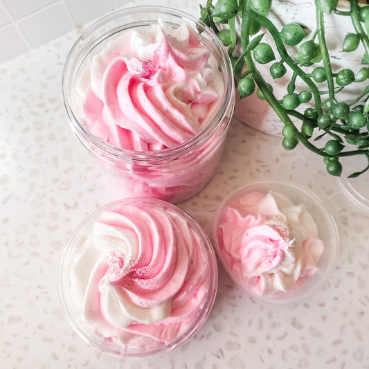 Pink and white whipped soap in clear containers on a light surface with greenery.