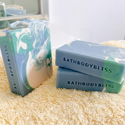 blue, green and white swirled soap bars with 'BathBodyBliss' branding on a textured surface.