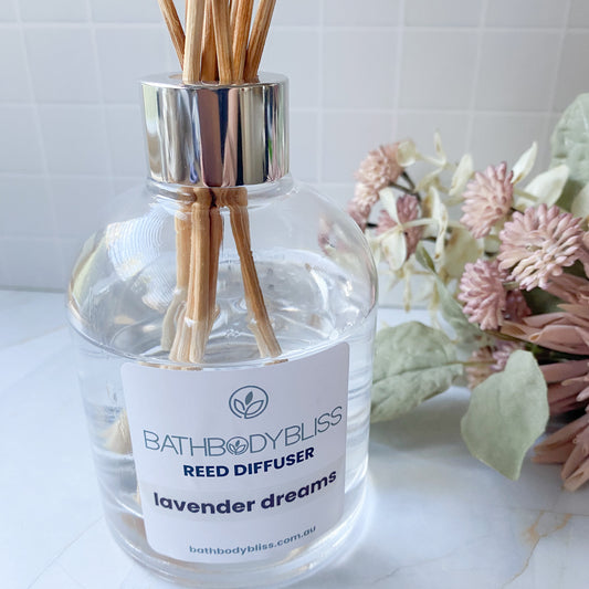 Bathbody Bliss reed diffuser labeled 'Lavender Dreams' with flowers in the background.