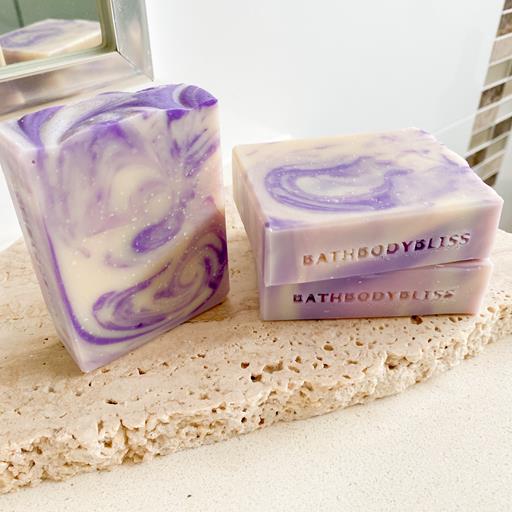 three bars of purple and white swirled handmade soap bars on a stone surface