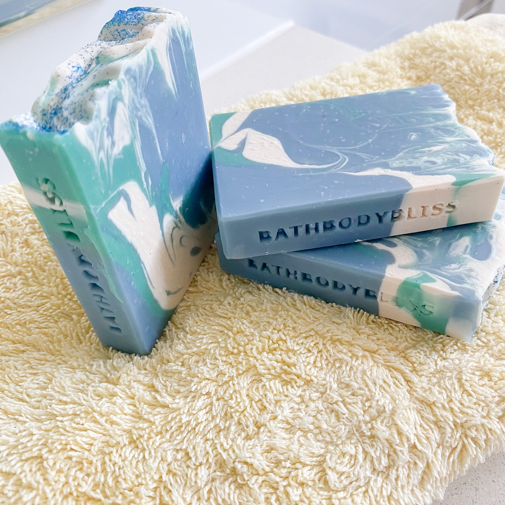 Three bars of Bathbodybliss soap on a textured surface