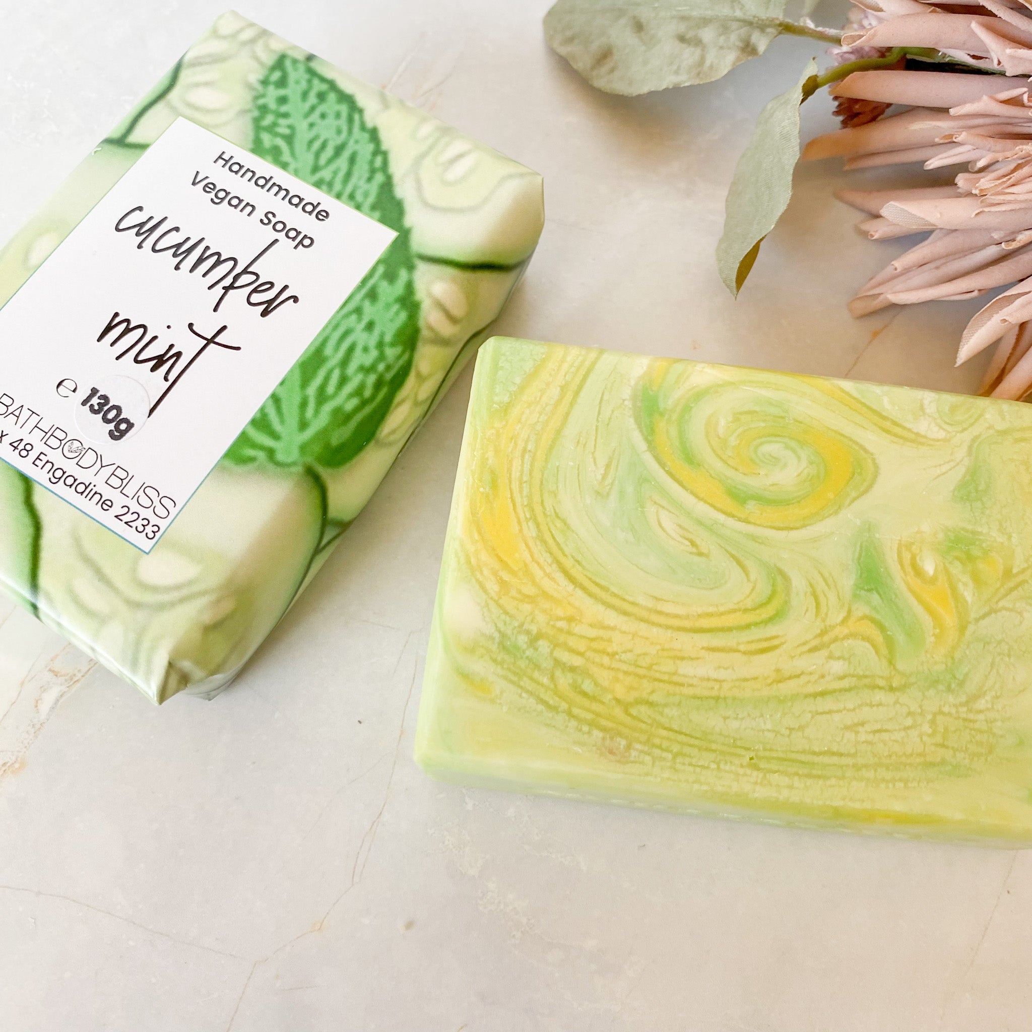 wrapped and unwrapped soap bars in swirls of green and yellow on a light background with floral decor