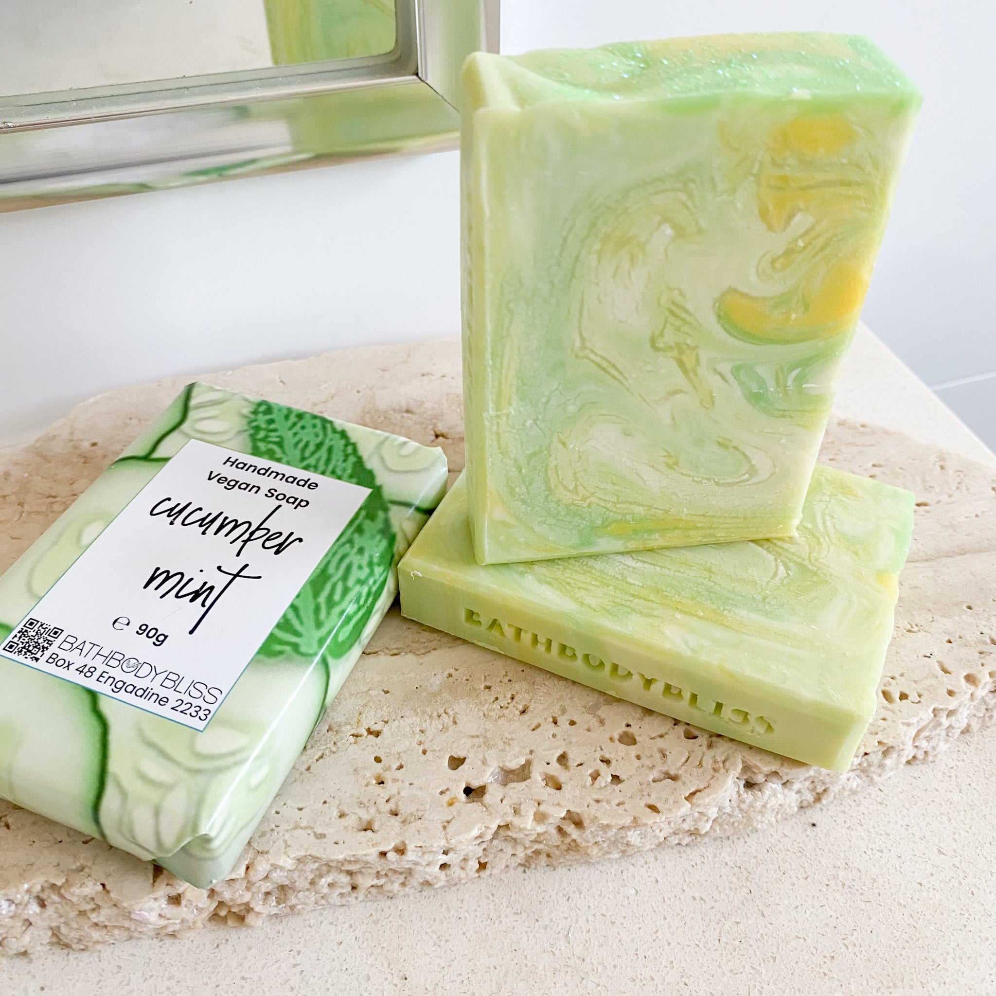 swirled green, yellow & white cucumber mint soap bars stacked on a light rock surface