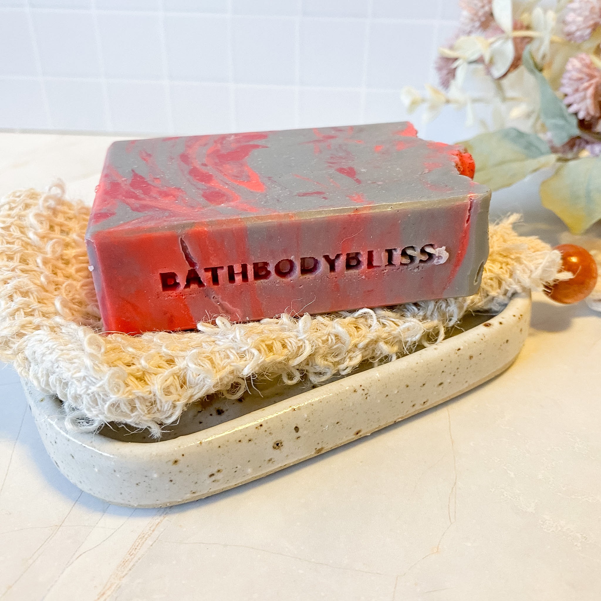 bar of grey and red swirled soap on a textured bag and pottery soap dish