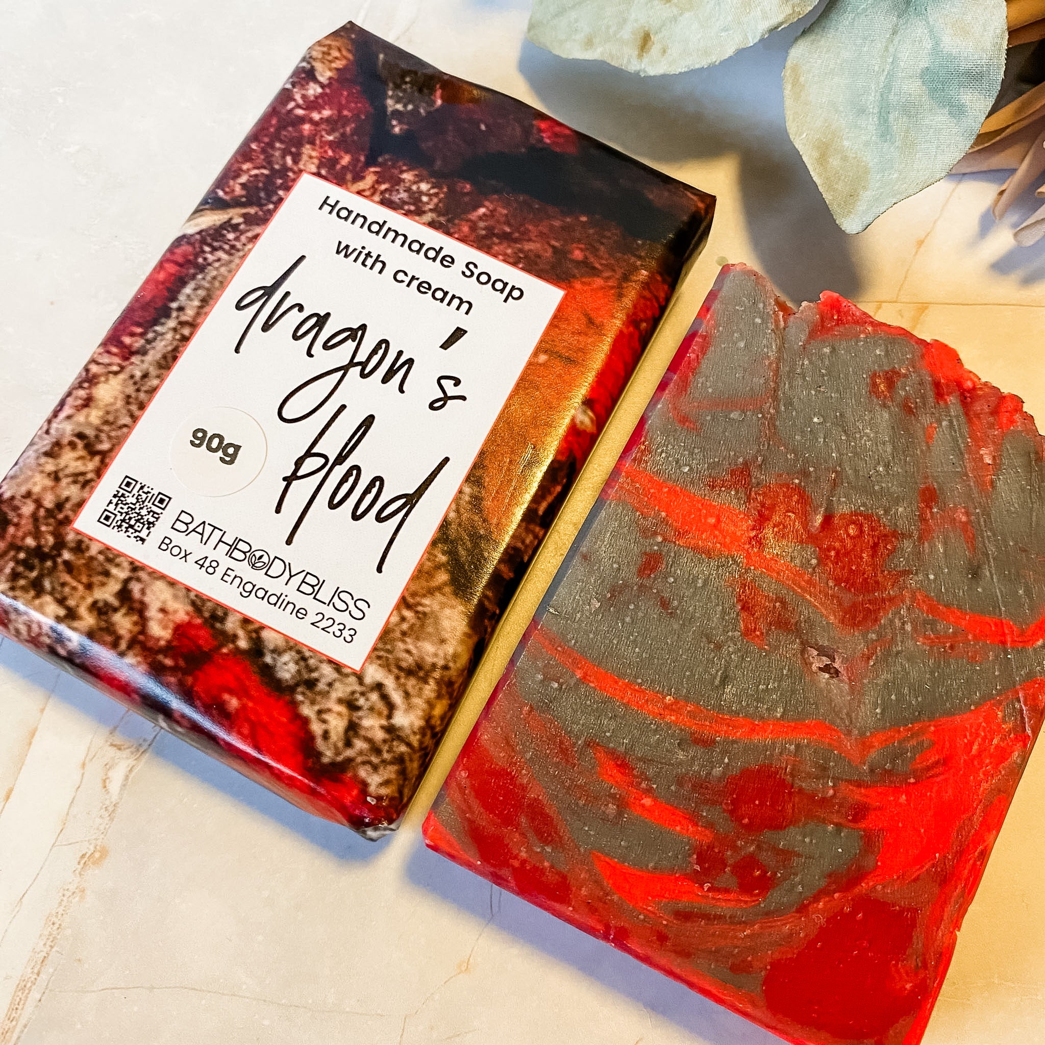 Handmade soap bar with 'Dragon's Blood' packaging on a textured surface.
