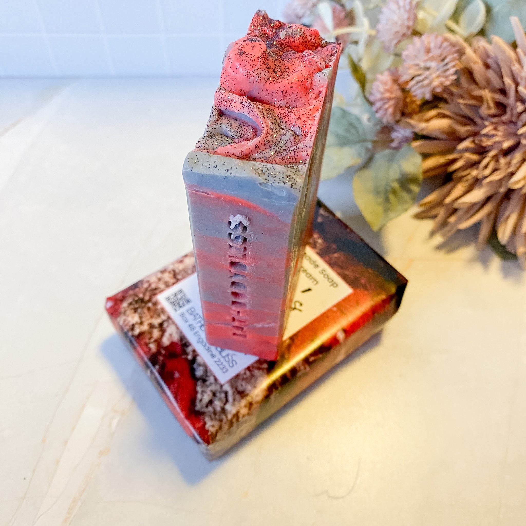 Decorative soap bar with a red and gray design on a light surface with flowers in the background