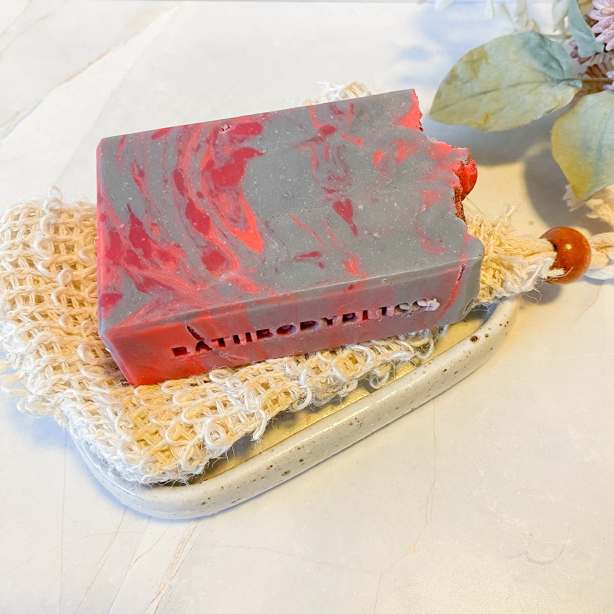Marbled red and gray soap bar on a textured surface with 'Bathory' branding.