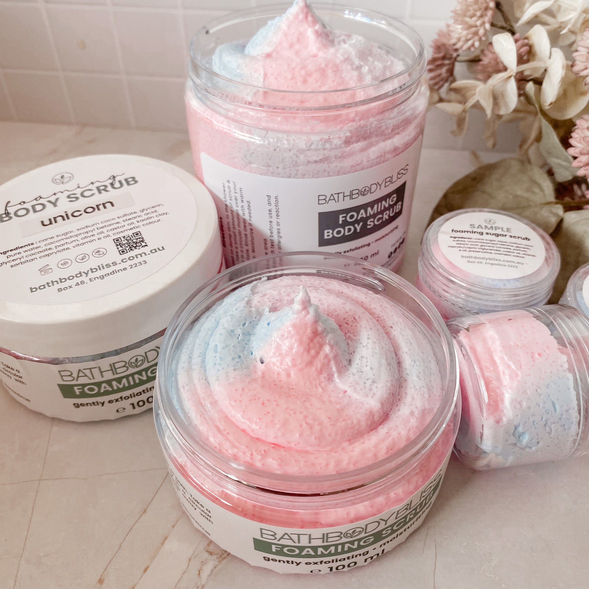 Jars of Bath Body Bliss foaming body scrub with visible brand labels on a bathroom counter.