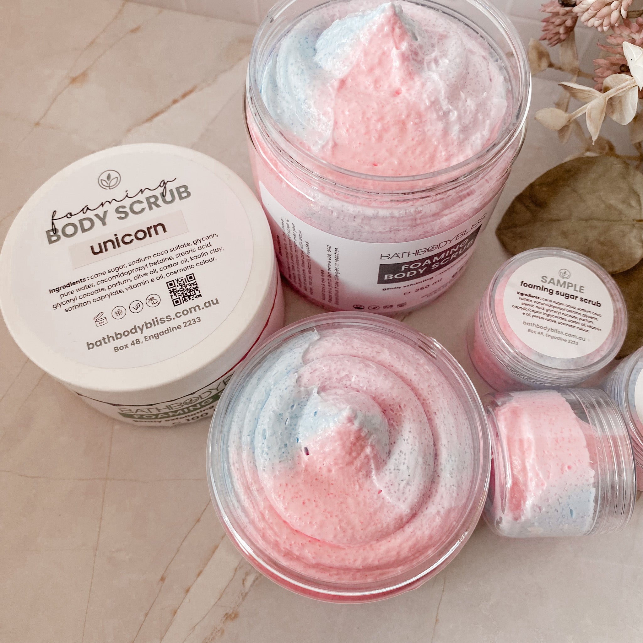 Foaming body scrub with pink and white texture in jars on a light marble surface.