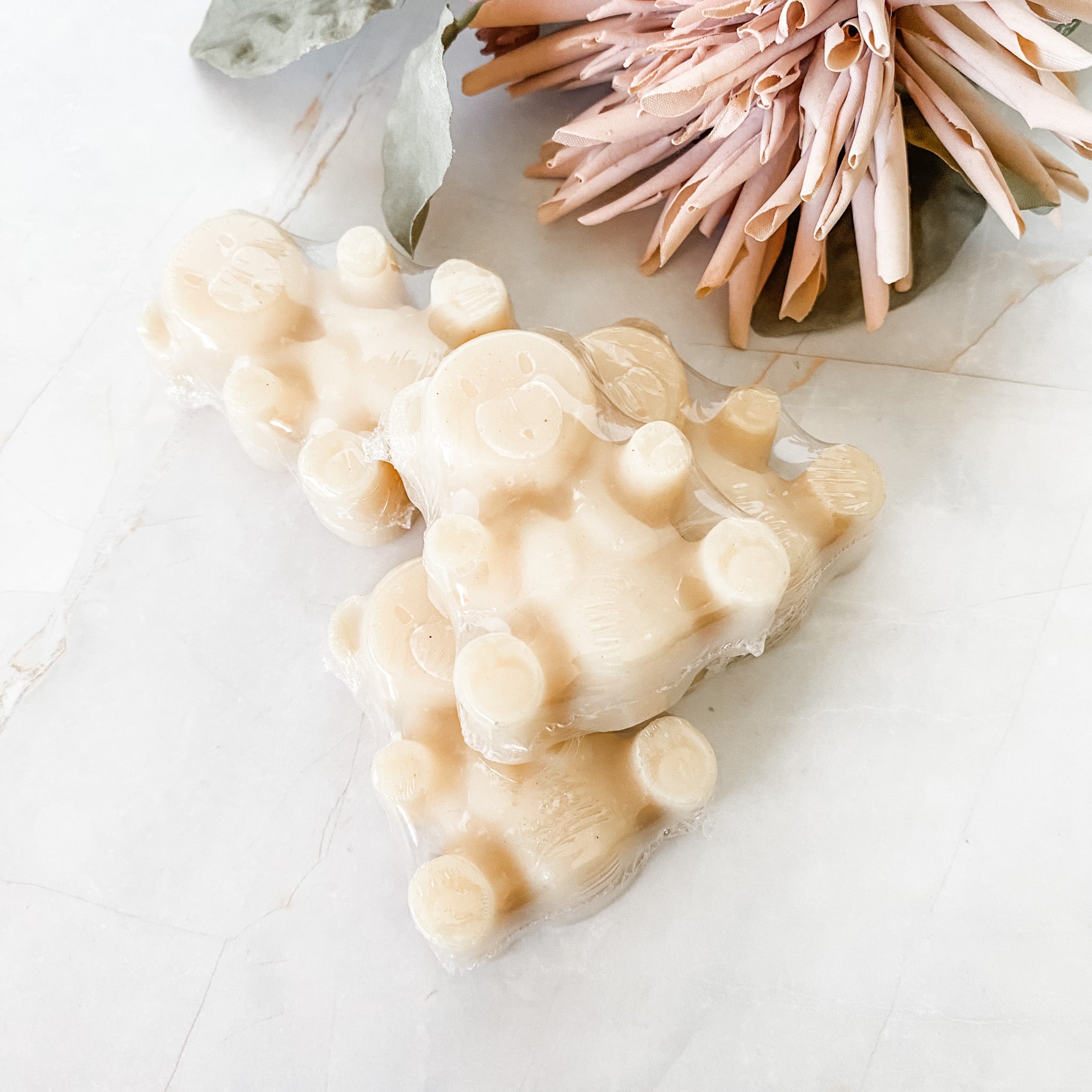 4 small teddy bear shaped creamy coloured soap bars on a white background with decorative elements