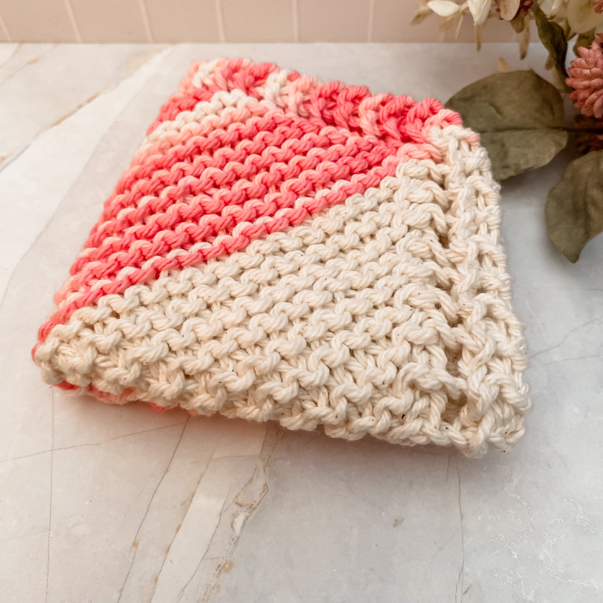 A hand-knitted multicolored cotton face or dish cloth laid out on a marble surface.