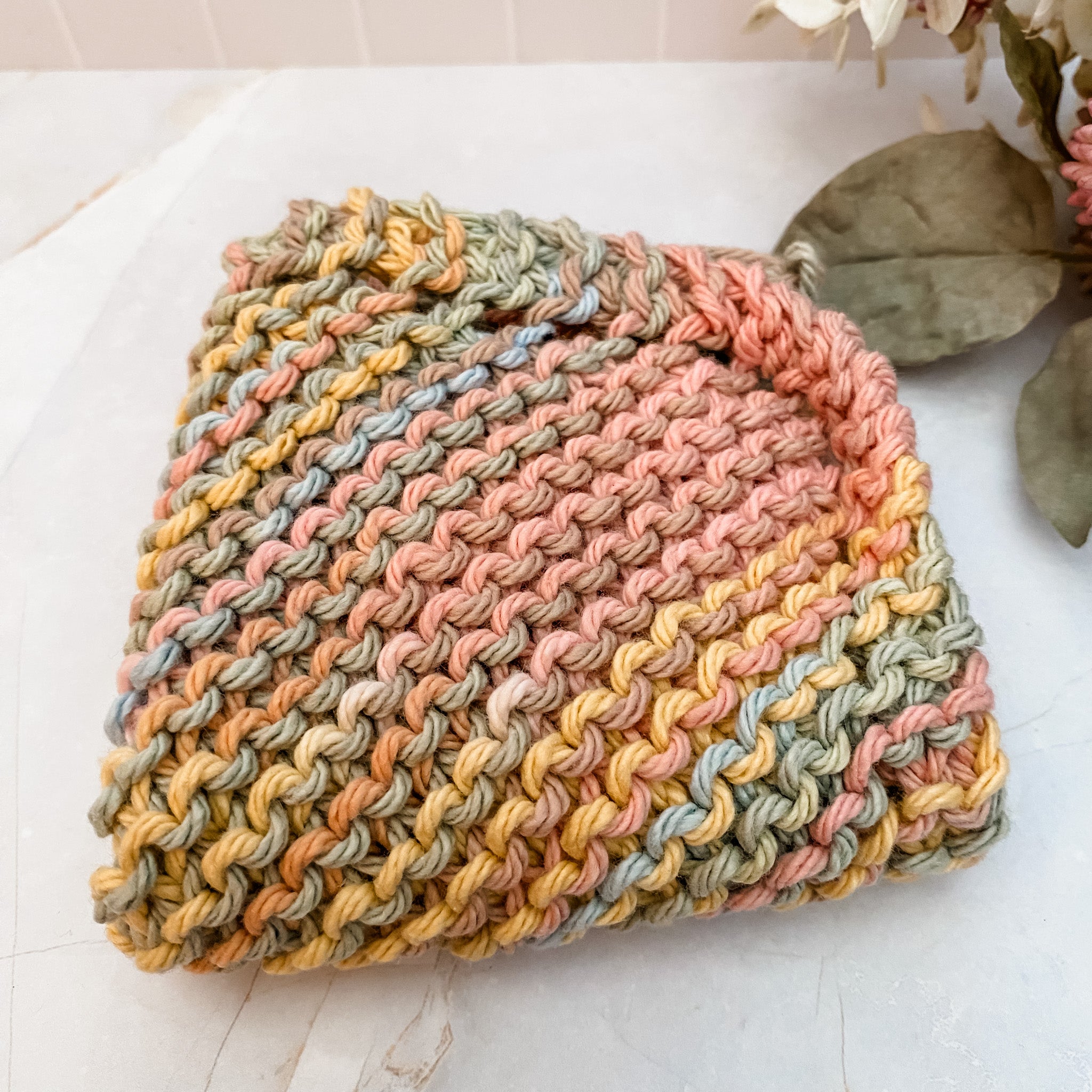 A hand-knitted multicolored cotton face or dish cloth laid out on a marble surface.