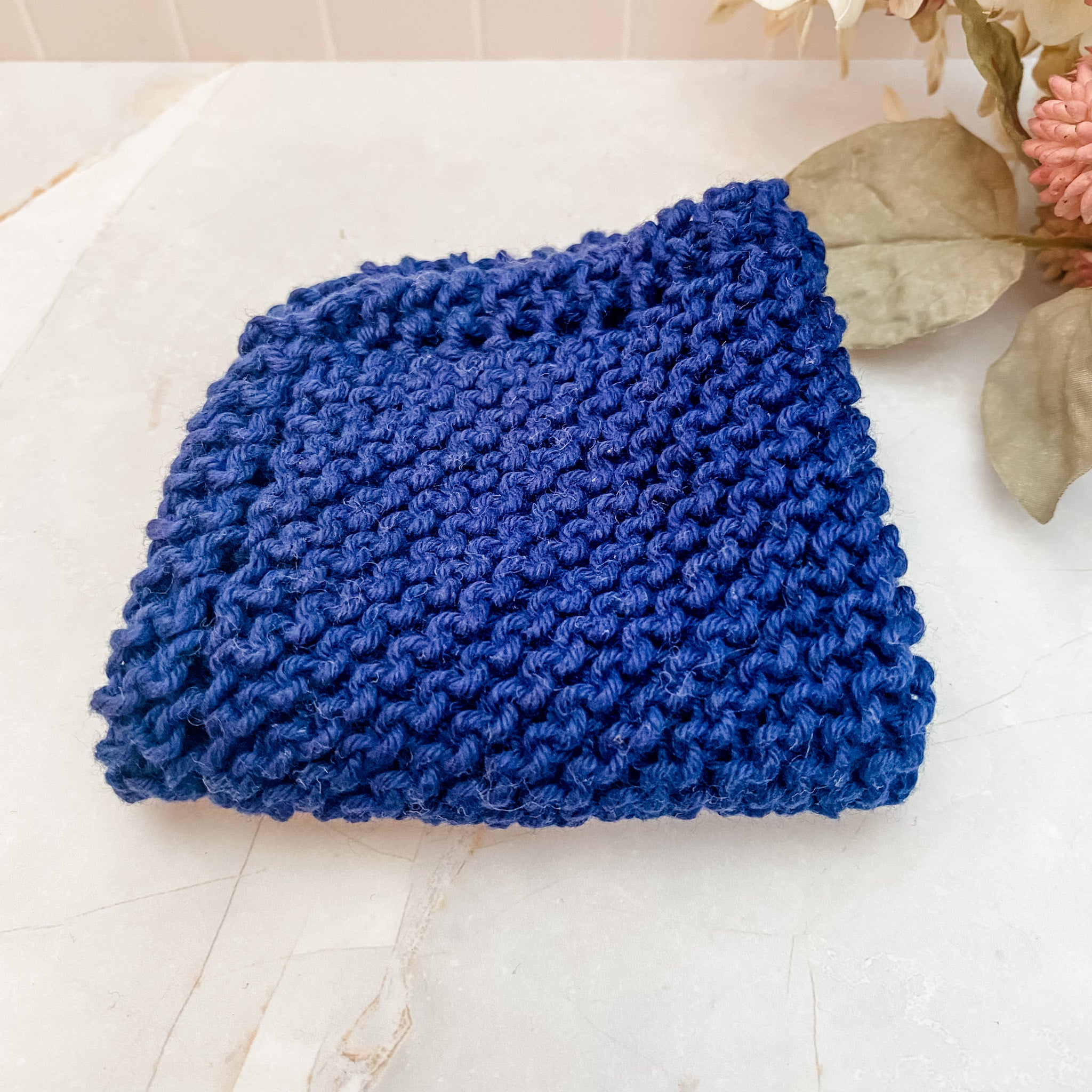 A hand-knitted blue cotton face or dish cloth laid out on a marble surface.