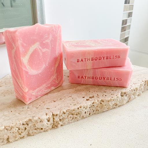Three bars of strawberry milk vegan soap with a pink and white marbled design, placed on a natural stone surface.