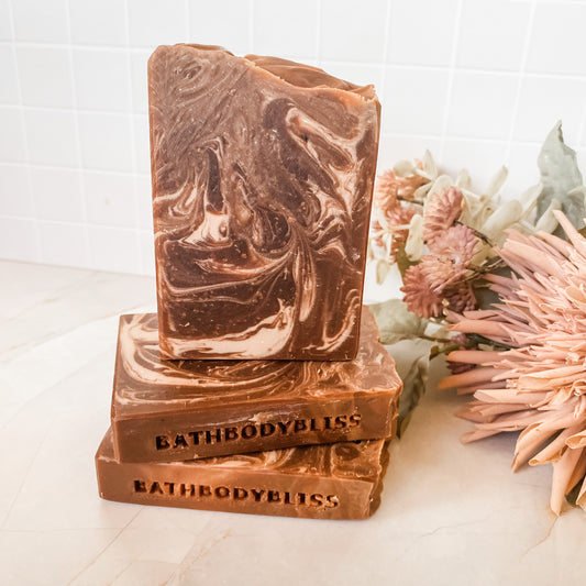 Stack of BathBodyBliss soap bars with a floral arrangement on a light background