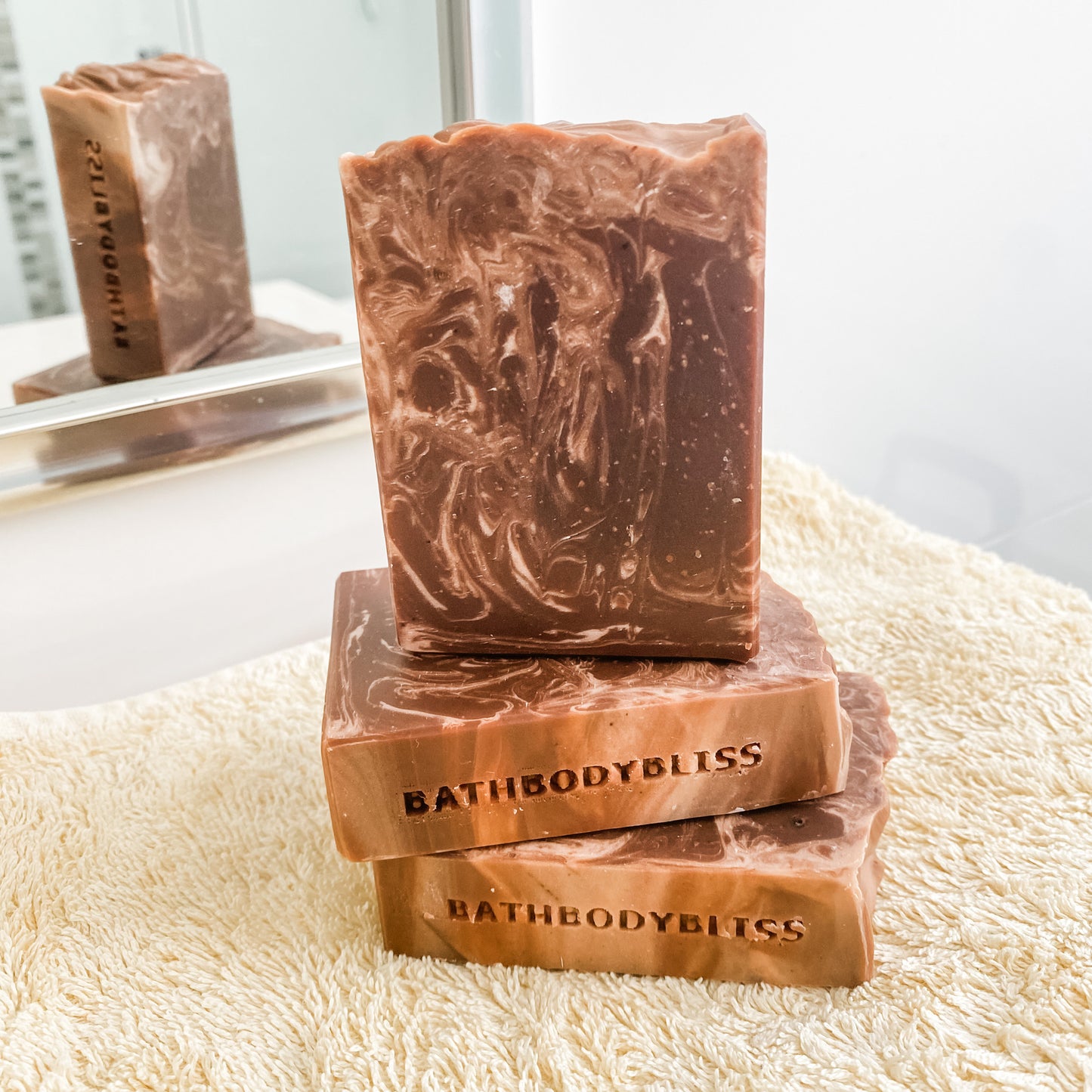 Three bars of BathBodyBliss soap stacked on a towel with a blurred background