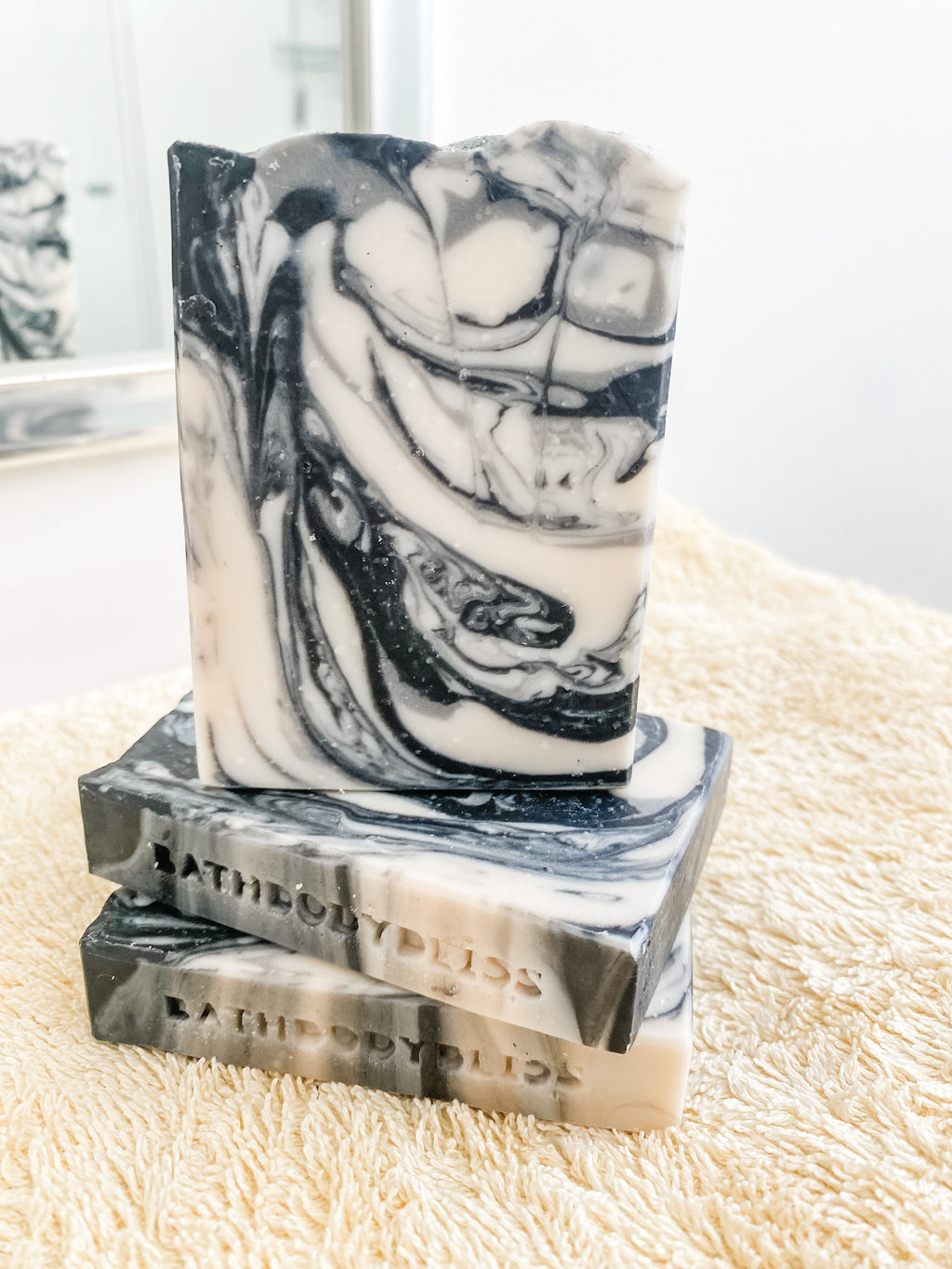 A bar of handmade vegan soap with a black and gray marbled pattern, placed on a textured surface.