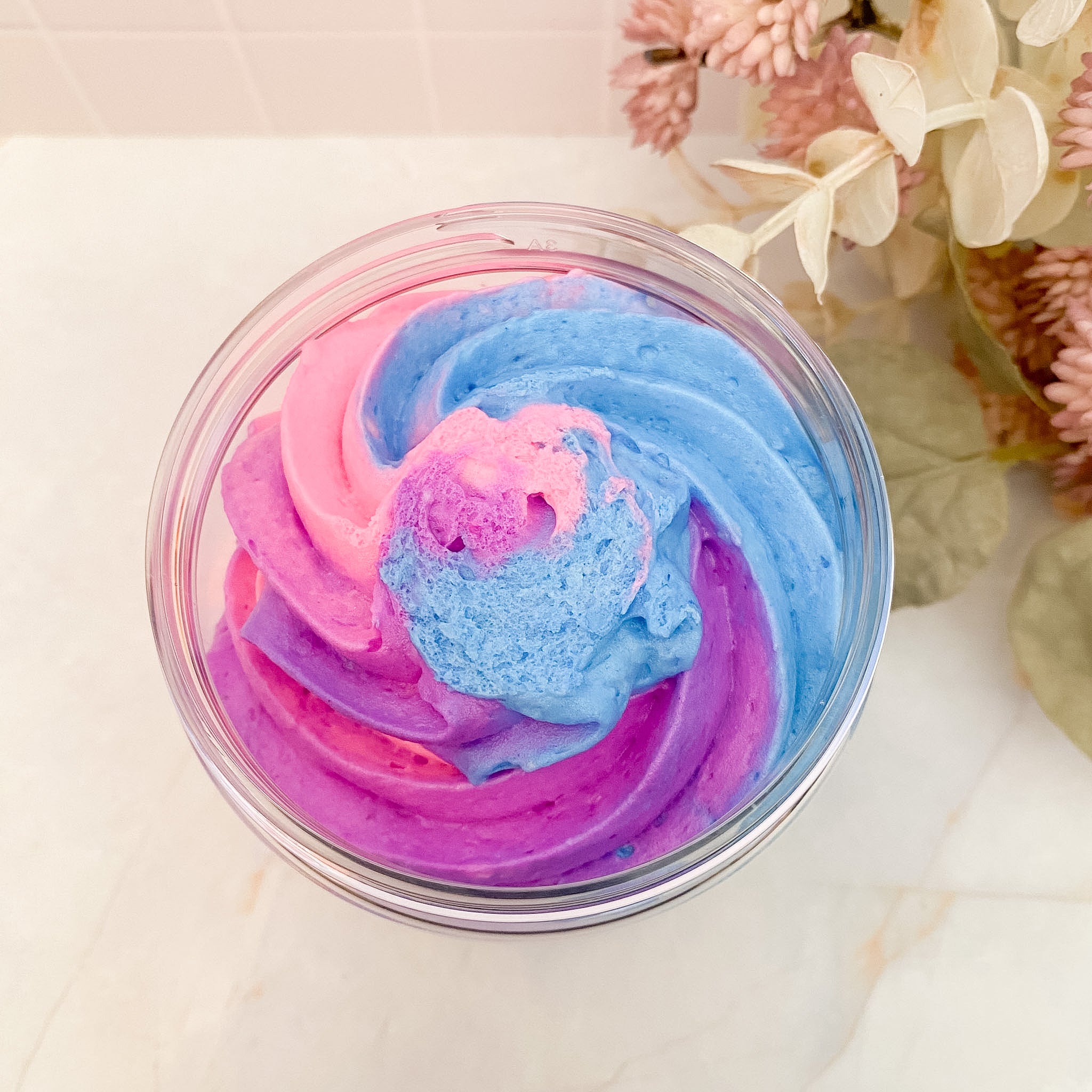 Colorful swirled soap in a clear container with flowers in the background