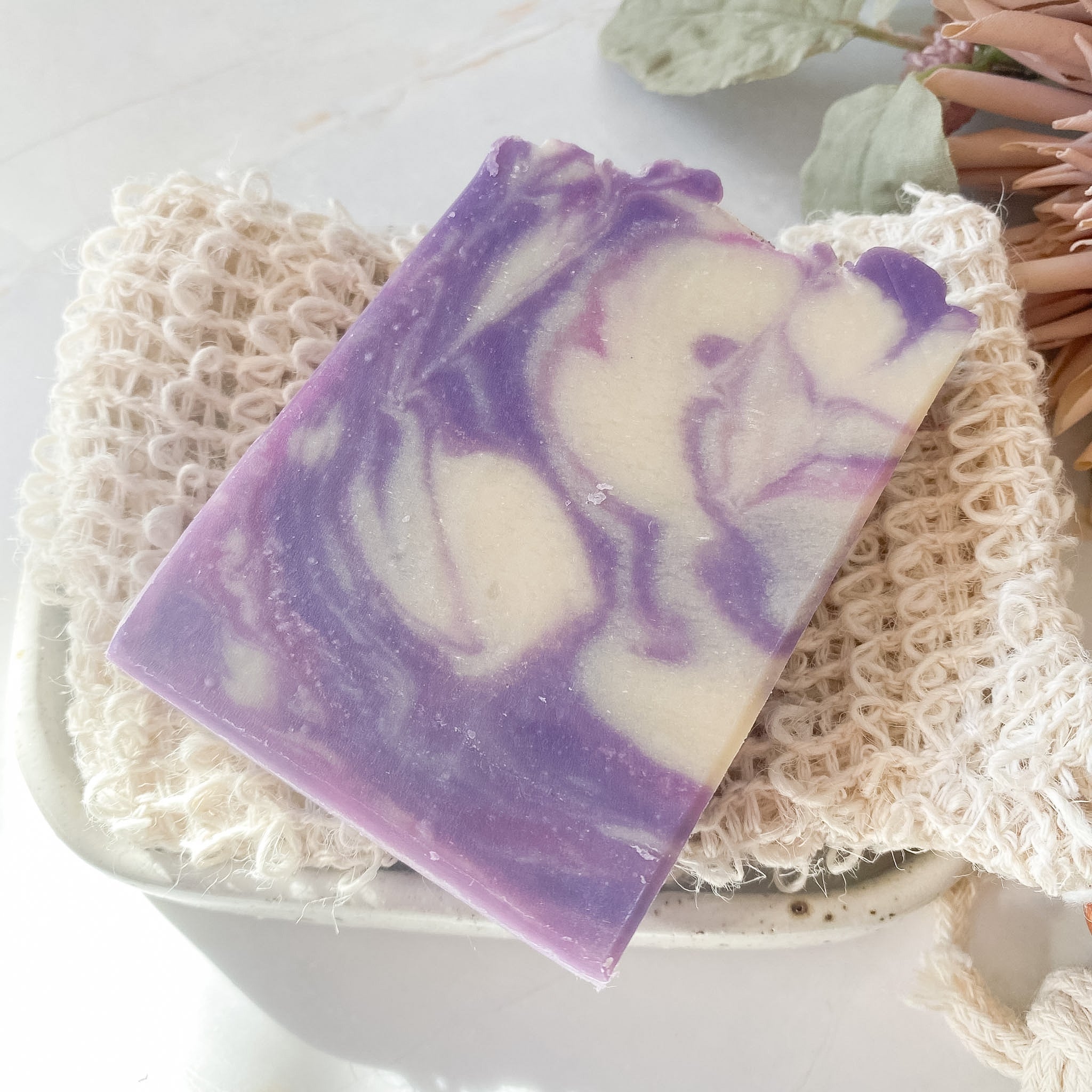 Purple and white soap bar on a loofah with a blurred natural background