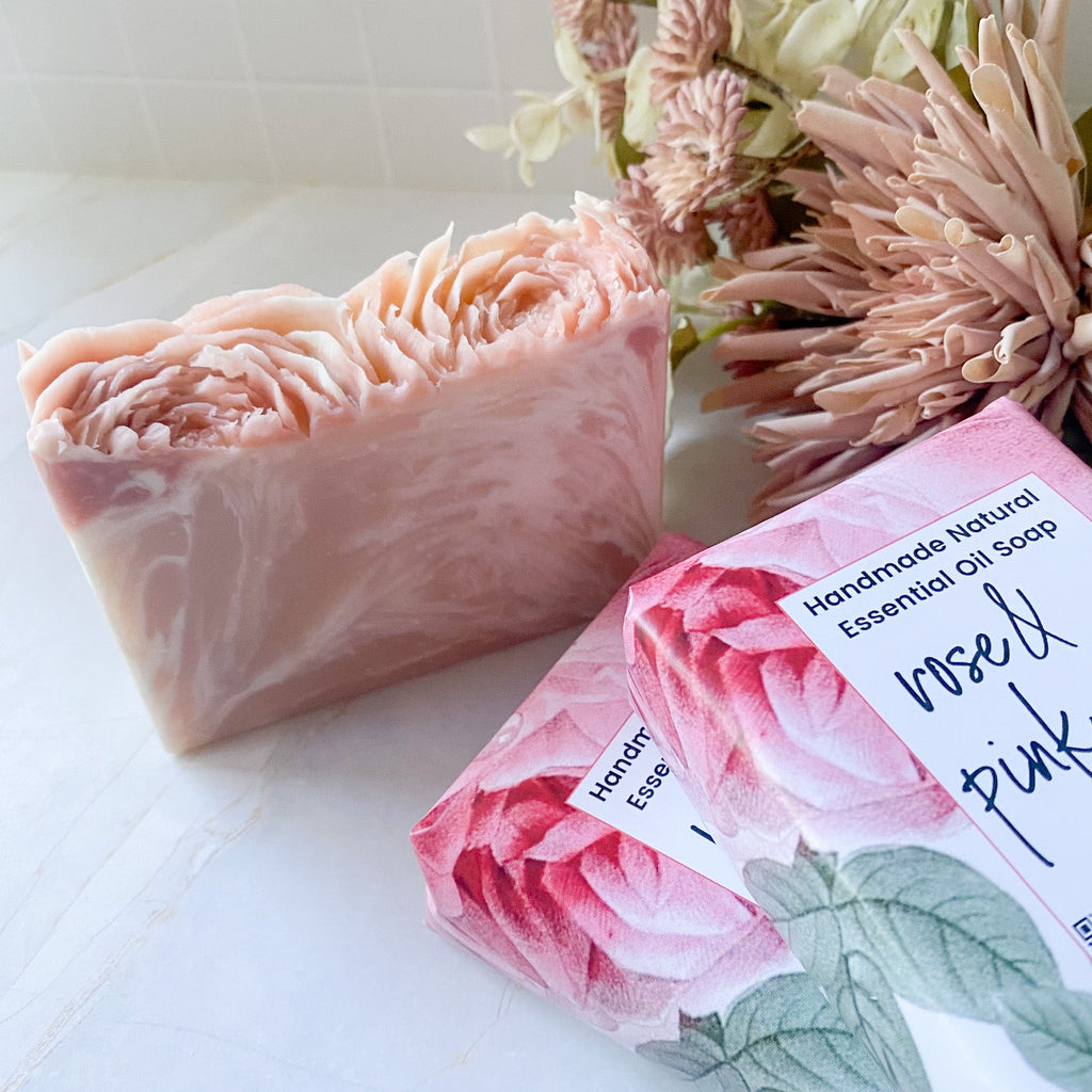 Pink handmade soap bar with packaging featuring floral design on a white surface.
