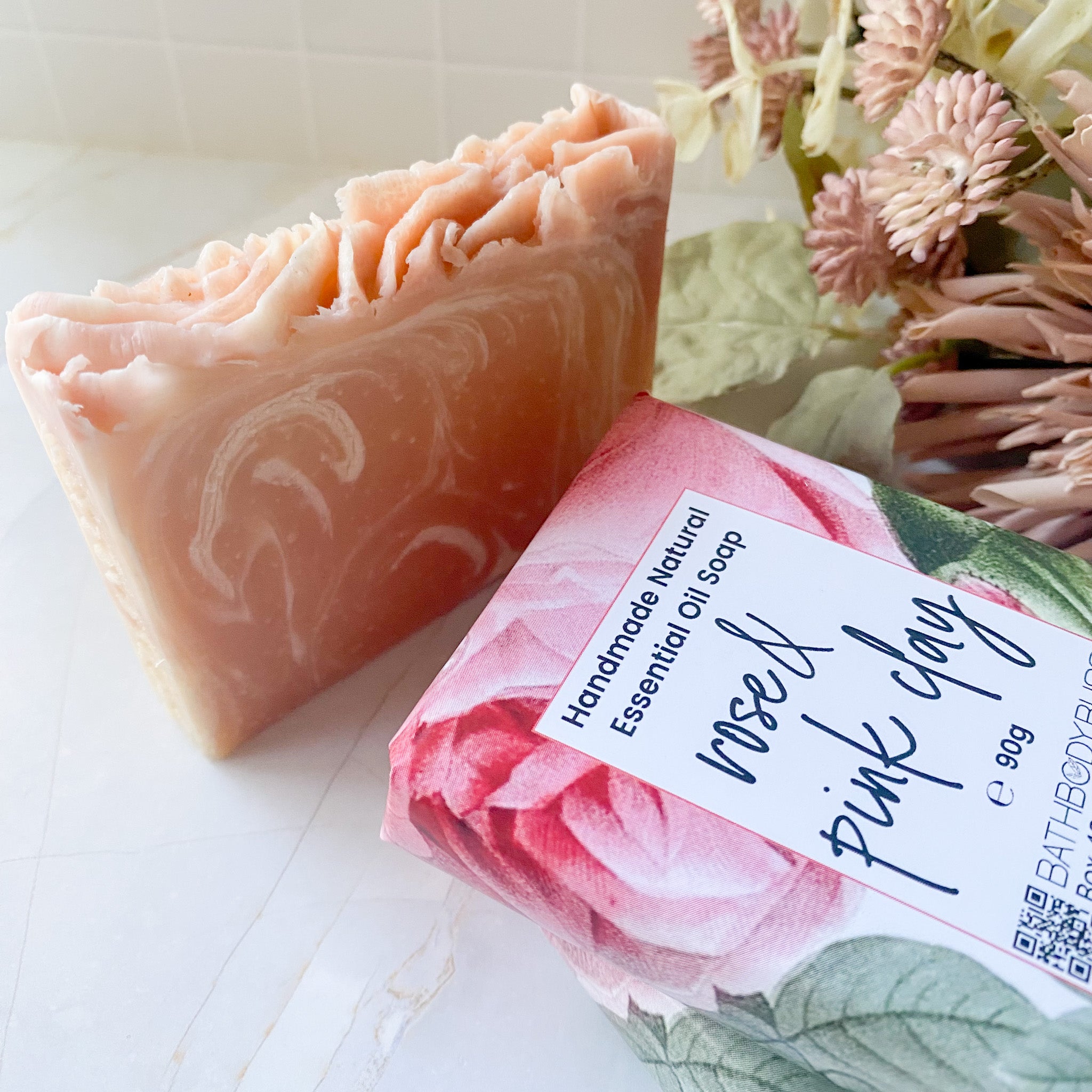 Handmade soap bar with a pink and white design next to its packaging featuring floral illustrations.