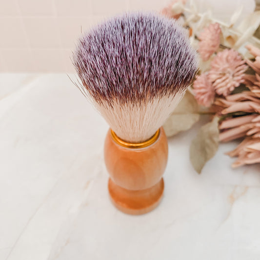 A shaving brush with natural bristles and a natural wood handle, displayed on a marble surface.