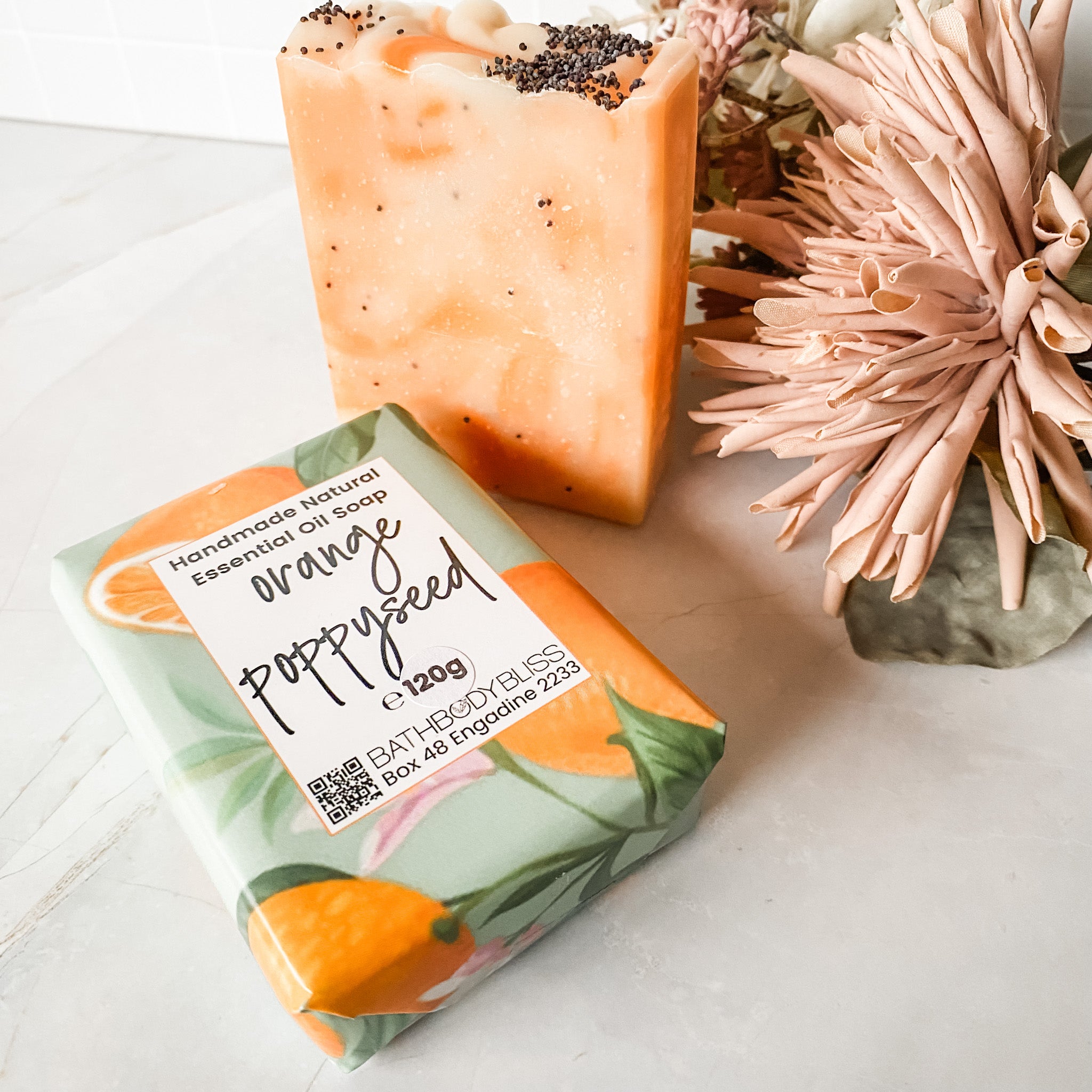 orange poppyseed soap bar in bath body bliss packaging and a standing unwrapped soap bar with orange swirls and poppyseeds on top next to it