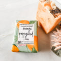 orange poppyseed soap bar in bath body bliss packaging and a standing unwrapped soap bar with orange swirls and poppyseeds on top next to it