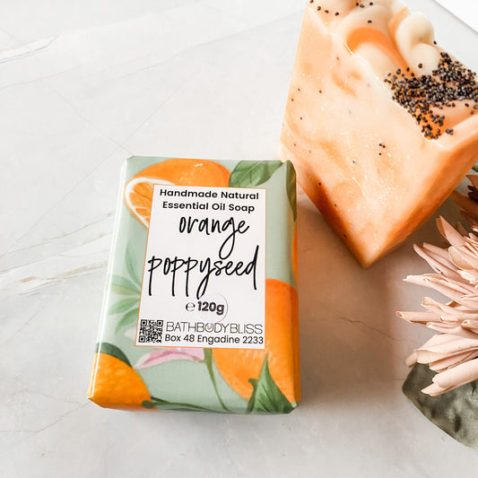 orange poppyseed soap bar in bath body bliss packaging and a standing unwrapped soap bar with orange swirls and poppyseeds on top next to it