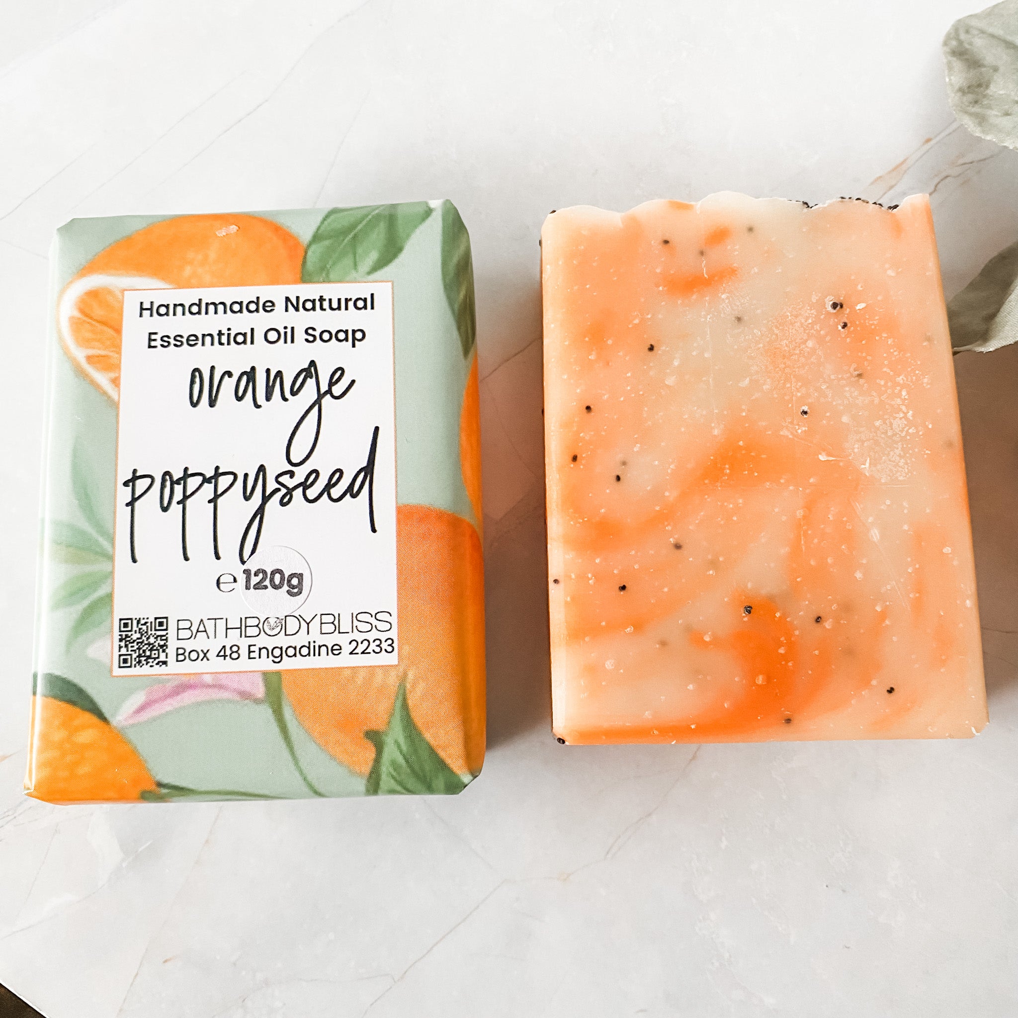 Orange poppyseed soap bar with and without bath body bliss branded packaging on a white background