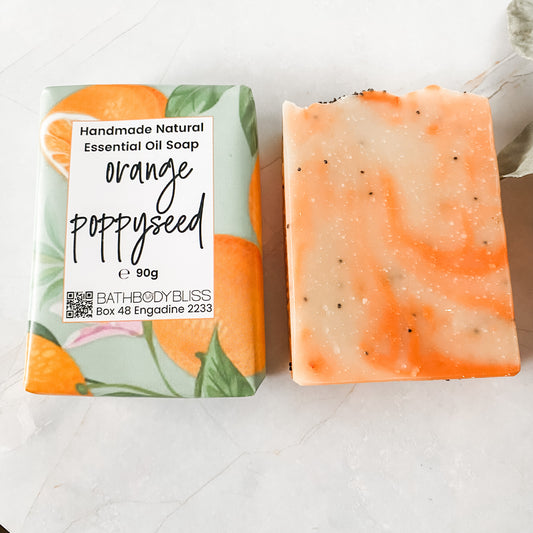 orange and cream swirled soap bar with poppyseeds in bathbodybliss branded paper wrap and unwrapped soap bar beside it on a white background