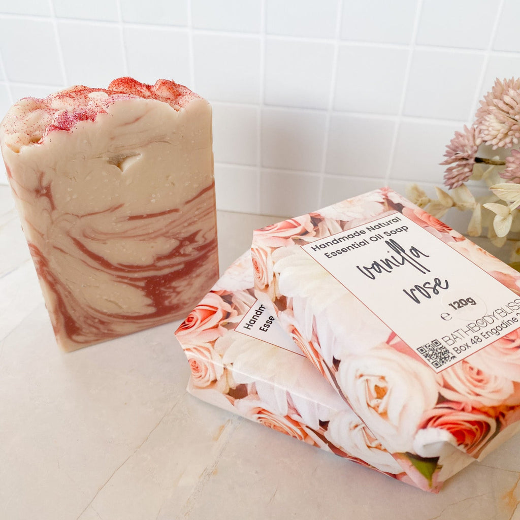 Three bars of soap, two wrapped and one unwrapped with a floral design, on a tiled bathroom floor.