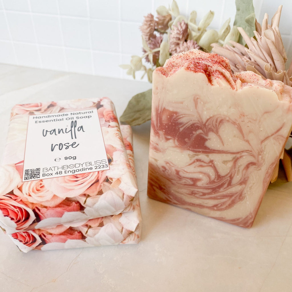 Three soap bars, two with a floral packaging label and the other with a marbled design, on a light surface.