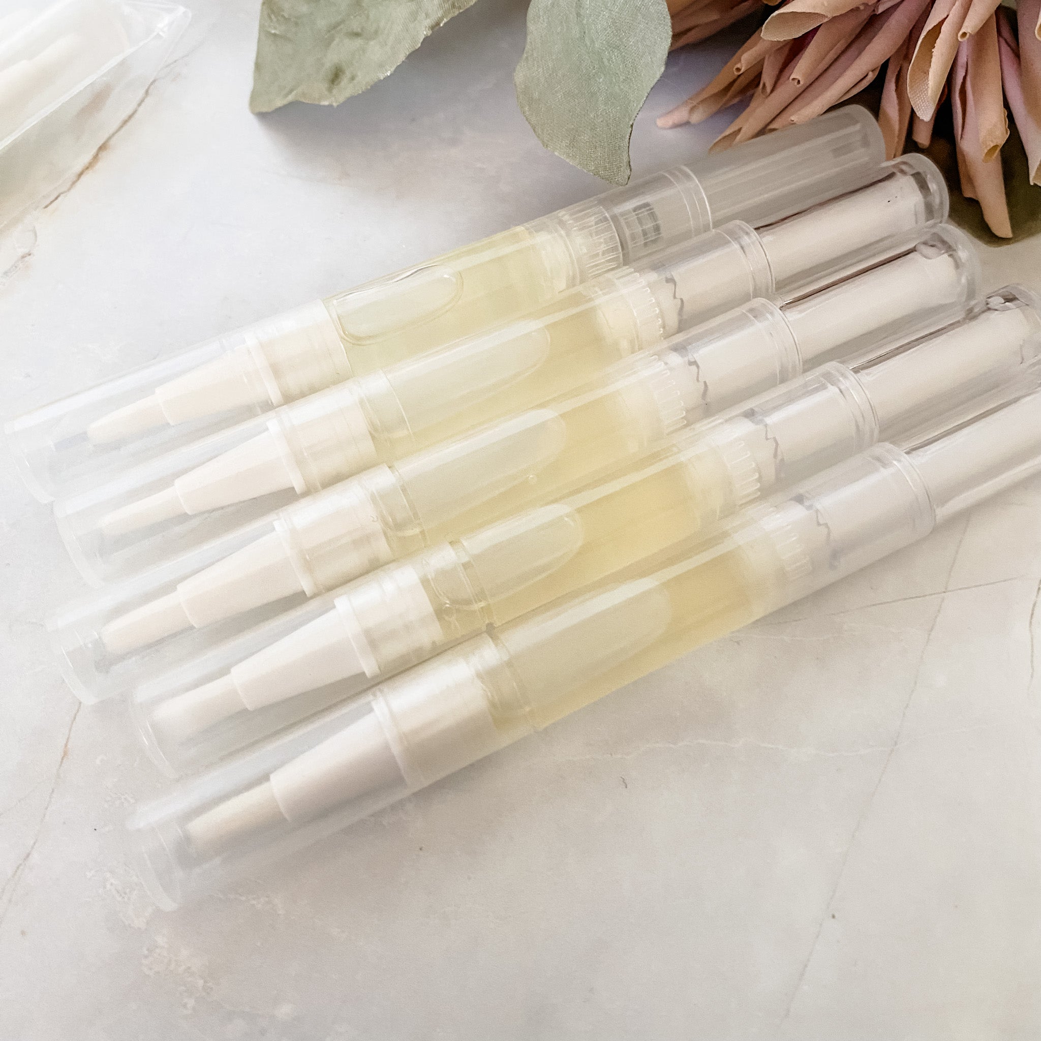 five twist up pens of cuticle oil on a light surface