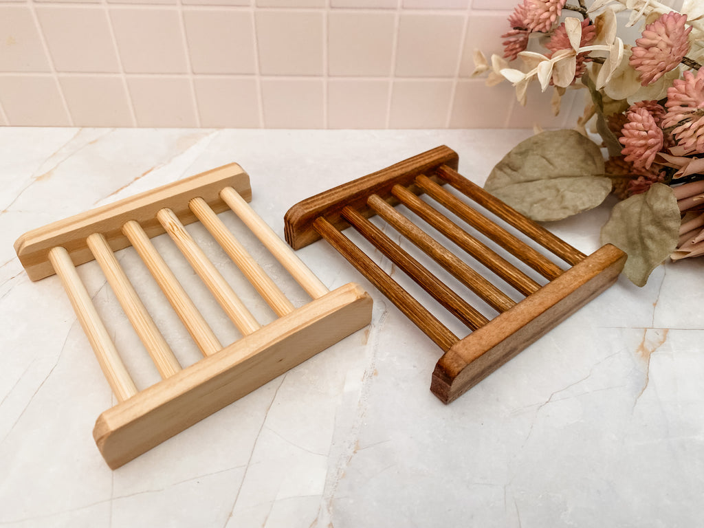 Two wooden soap dishes on a bathroom counter with a floral arrangement in the background.