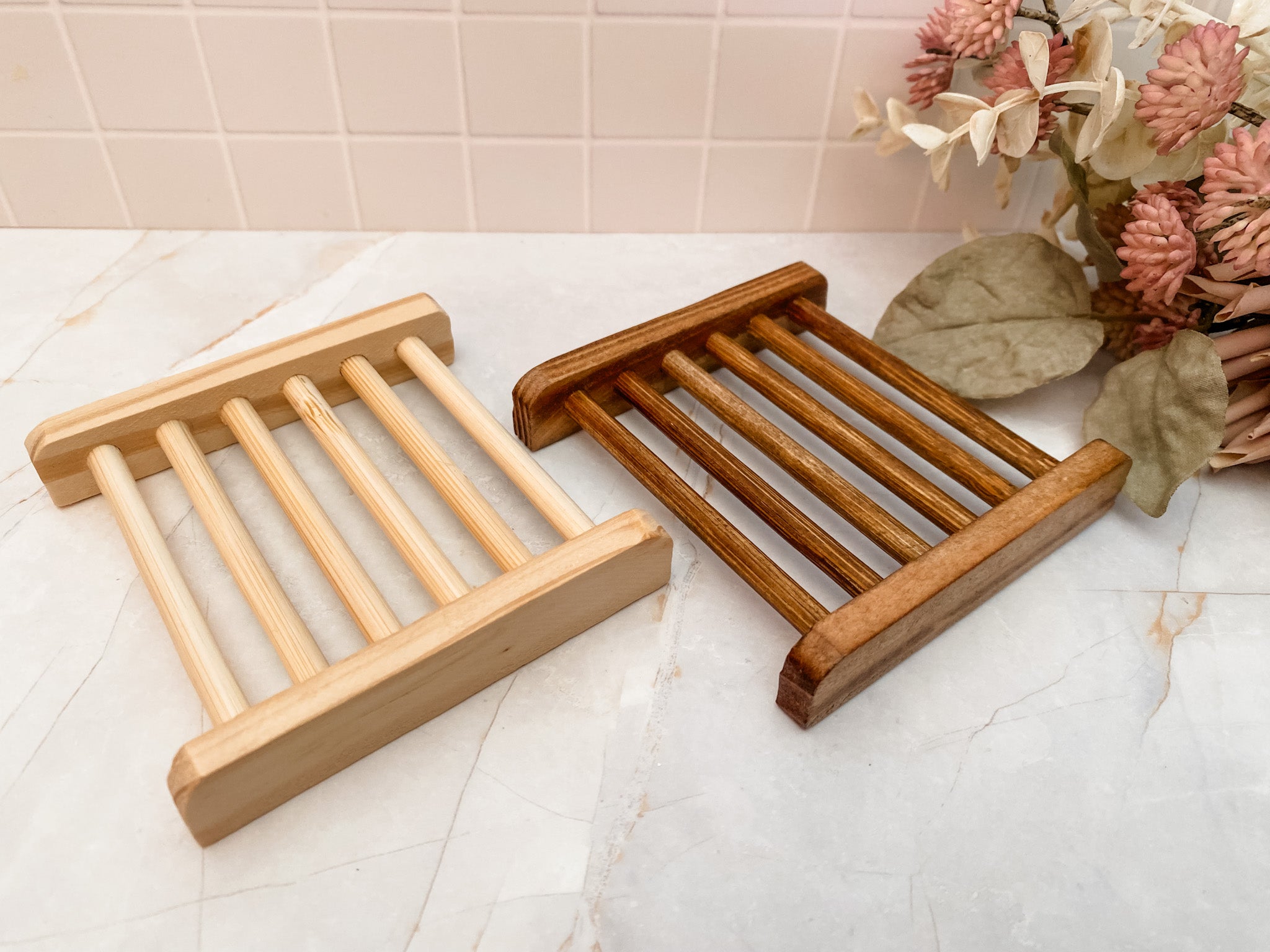 Two wooden soap dishes on a bathroom counter with a floral arrangement in the background.