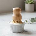 Bamboo dish brush with placed on top of a white ceramic dish soap container, on a white marble kitchen bench