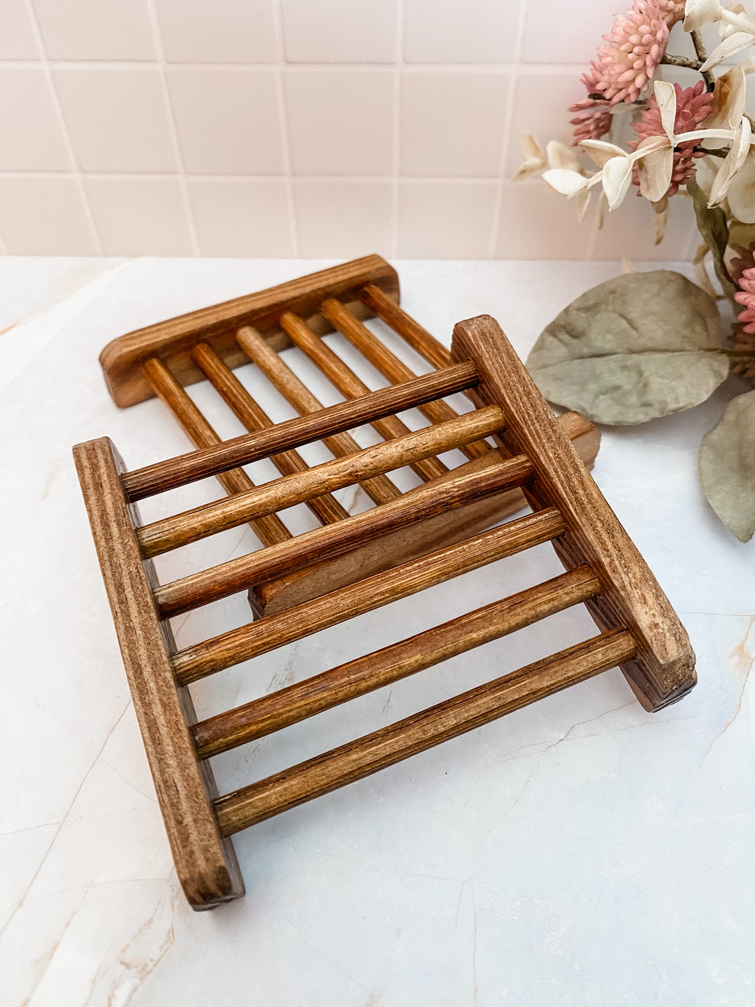 square bamboo soap dishes placed on a marble surface, with a few leaves in the background.
