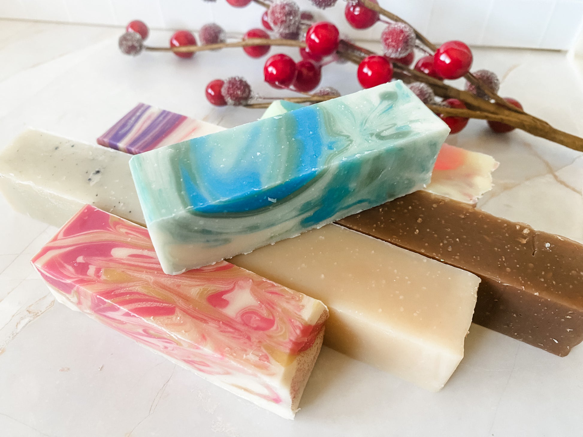 Colorful soap bars on a white surface with red berries in the background