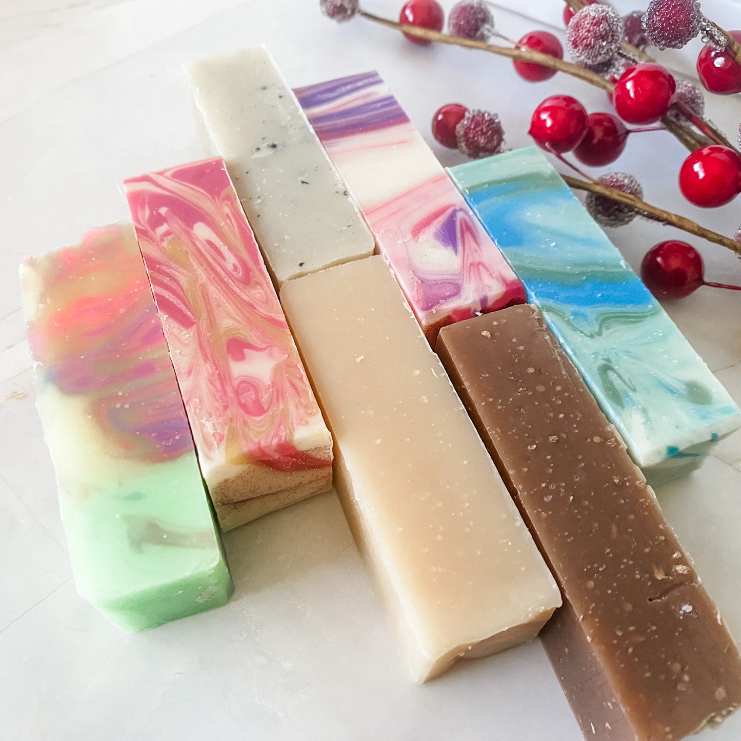 Colorful soap bars on a white surface with red berries in the background