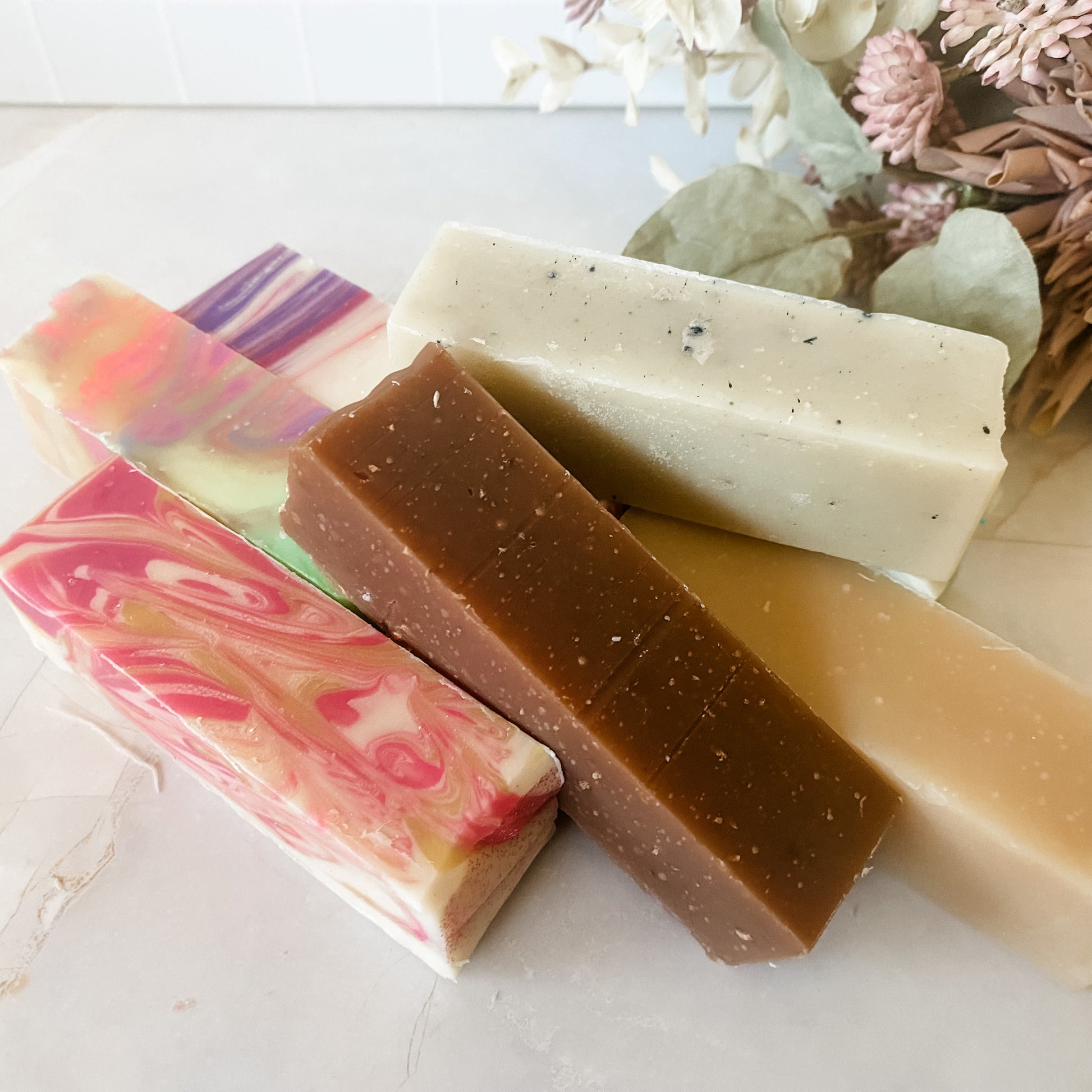 Six different colored soap bars on a light surface with decorative elements.