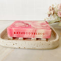 Pink marbled soap bar with 'BATHBODYBLISS' text on a speckled ceramic tray.
