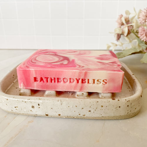 Pink marbled soap bar with 'BATHBODYBLISS' text on a speckled ceramic tray.