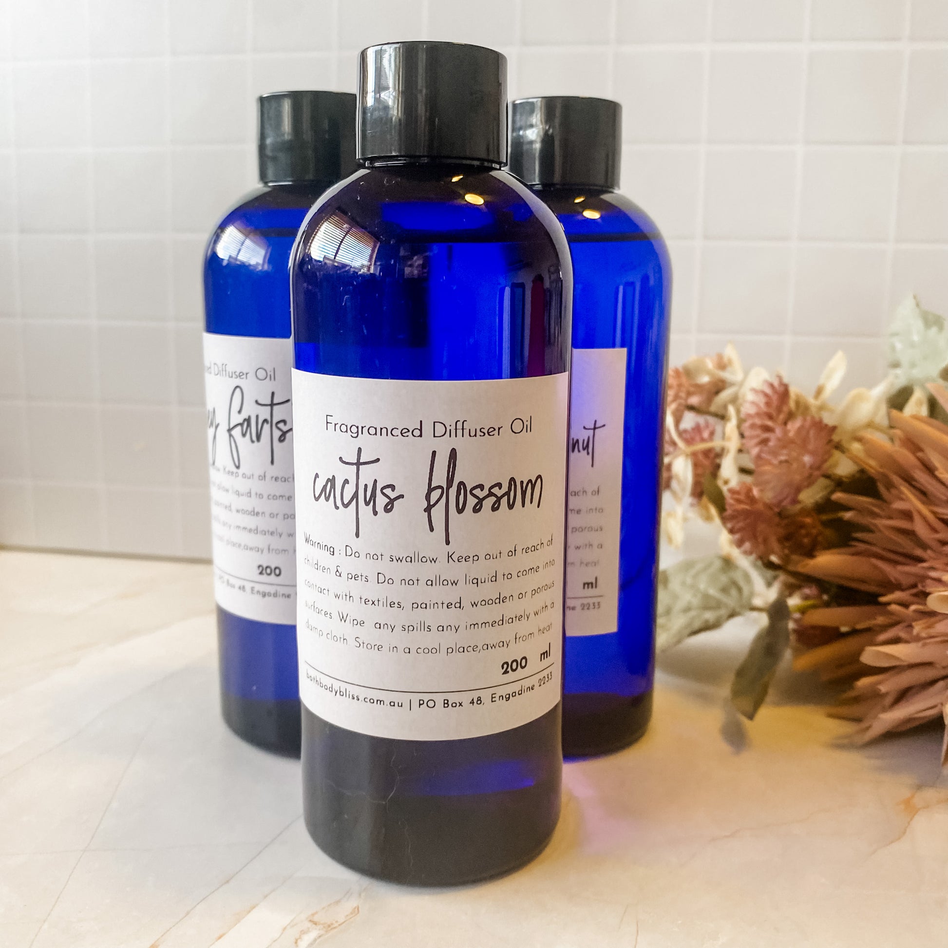 Three blue bottles of diffuser oil on a light surface with a decorative plant in the background.