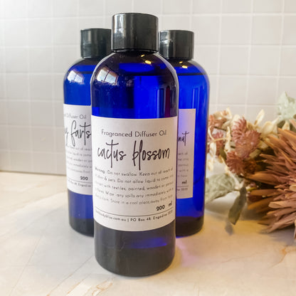 Three blue bottles of diffuser oil on a light surface with a decorative plant in the background.