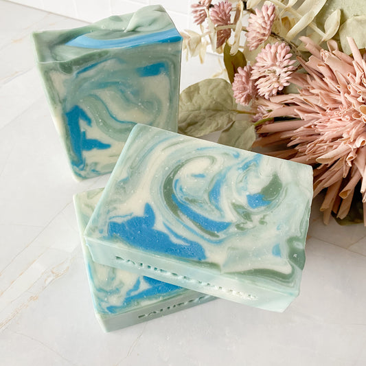 Three swirled soap bars with blue and green colors on a white surface with decorative flowers.