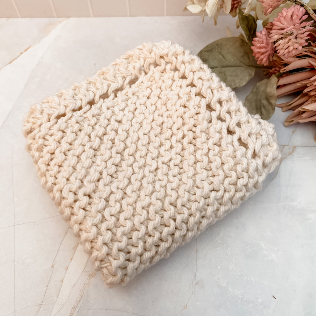 A hand-knitted ivory cotton face or dish cloth laid out on a marble surface.