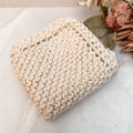 A hand-knitted ivory cotton face or dish cloth laid out on a marble surface.