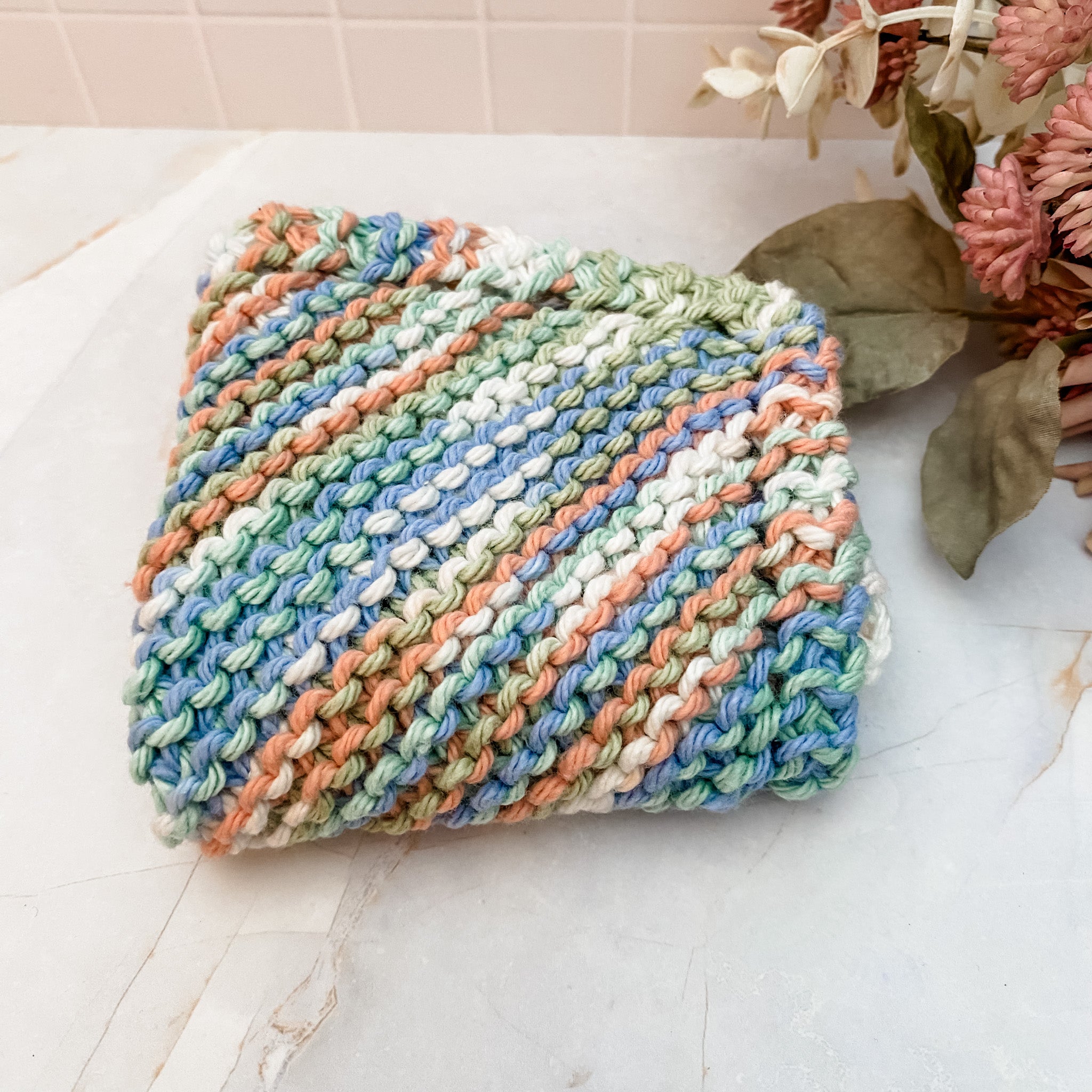 A hand-knitted multicolored cotton face or dish cloth laid out on a marble surface.