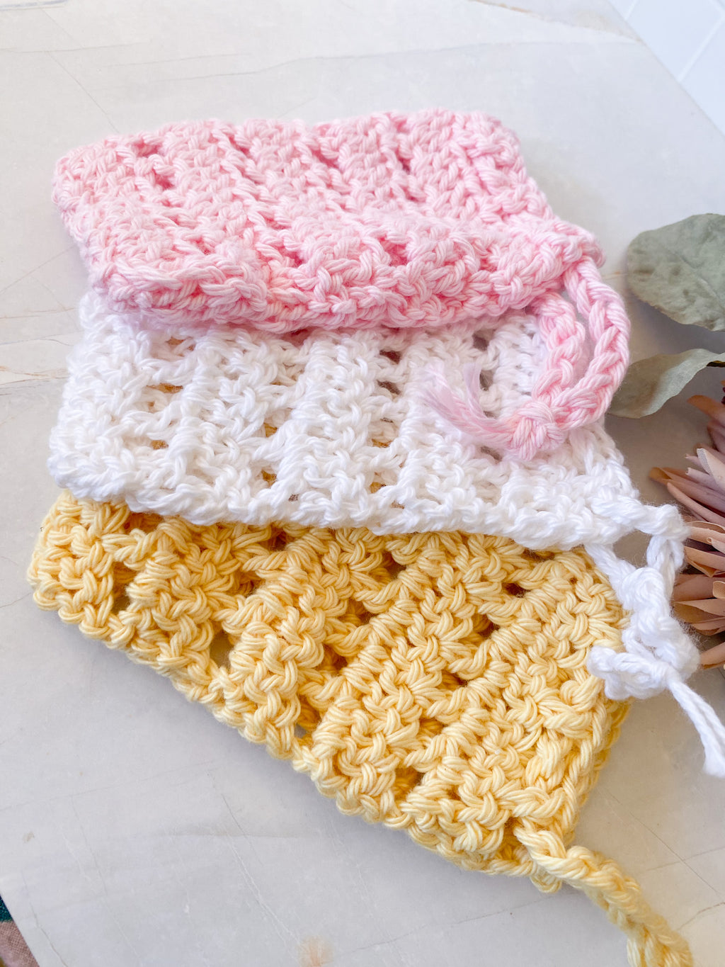 Stack of colorful crocheted soap saver sacks on a white surface